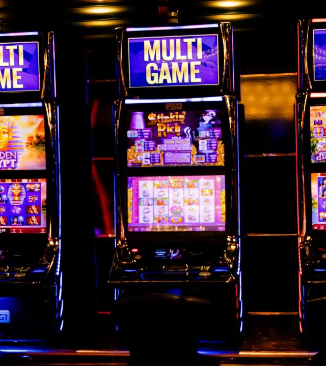 Three illuminated slot machines in a bustling casino at night.